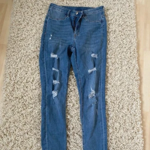 Blå ripped skinny jeans - Snygga blå jeans med flera slitningar och hål på framsidan av benen. Modellen är skinny med normal passform. Perfekta för dig som gillar en trendig stil!