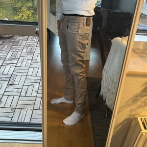  Replay Anbass jeans slim fit - Säljer ett par snygga beige Replay Anbass jeans med slim fit och klassisk femficksdesign. Jeansen har tydliga sömmar, läderpatch med Replay-logga bak och är tillverkade i mjukt bomullsmaterial med lite stretch för extra komfort.