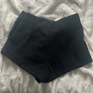 Svarta shorts - Säljer ett par svarta shorts med stilren och enkel design. Shortsen har en diskret dragkedja i sidan och är sydda i ett lite tjockare tyg som ger en snygg form. Perfekta för dig som gillar minimalistisk stil!💕