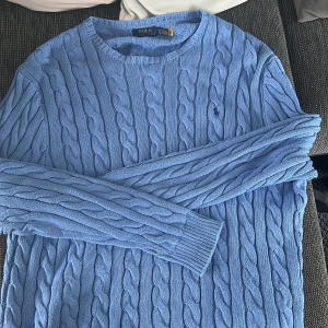Blå kabelstickad tröja Polo Ralph Lauren - Kabelstickad tröja i ljusblått från Polo Ralph Lauren. Klassisk rund halsringning, långärmad och med broderad logga på bröstet. Tröjan är stickad i bomull, endast använd 3 gånger, nypris är 2395kr.