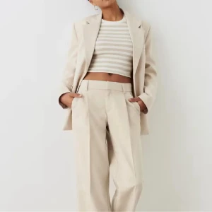 Beiga kostymbyxor från Gina Tricot - Stilrena beiga kostymbyxor från Gina Tricot i storlek S. Byxorna har medelhög midja, pressveck framtill, hällor för bälte och en dekorativ bakficka. Perfekta för en clean och snygg look.