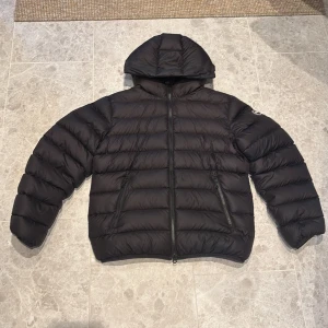 Svart dunjacka från Colmar med luva - Säljer en svart dunjacka från Colmar med luva och dragkedja. Jackan är quiltad och har två fickor med dragkedja framtill. Perfekt för kalla dagar och har en clean, sportig look. Passformen är normal och jackan är riktigt lätt och smidig att bära. jackan är i 10/10 skick och har knappt använts. Tveka inte att skriva för fler frågor!