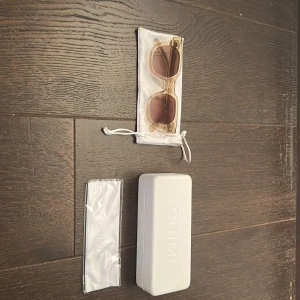 Ecru solglasögon från CHIMI - Snygga solglasögon från CHIMI med transparent beige båge och fyrkantig form. Glasen är bruna med en lätt toning. Kommer med originalfodral och putsduk. Perfekt accessoar för att lyfta din stil i solen.