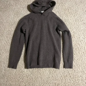 Mörkgrå hoodie i merinoull från Vailent - Mysig mörkgrå hoodie från Vailent i mjuk merinoull. Tröjan har huva, långa ärmar och ribbade muddar vid ärmslut och nederkant. Perfekt för dig som gillar stilrena och bekväma plagg med lite extra värme.