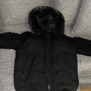 Svart pufferjacka Glorious Gangsta S - Svart pufferjacka från Glorious Gangsta i storlek S. Jackan har ett snyggt geometriskt mönster på axlar och huva, dragkedja framtill och broderad logga. Materialmix med vadderad polyester och detaljer i sammet. Perfekt för kalla dagar.