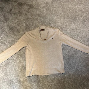 Beige stickad tröja med half zip Morris - Snygg beige stickad tröja från Morris med half zip och liten broderad logga på bröstet. Passar dig som är mellan 175-185. Pris kan diskuteras vid snabb affär.