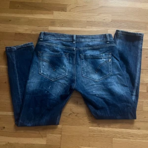 Blå jeans från Dondup med slitningar - Snygga blå jeans från Dondup med coola slitningar. Klassisk femficksmodell med dragkedja och raka ben. Jeansen är tillverkade i bomull och har en mörk tvätt med ljusa detaljer.
