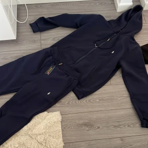 Marinblå hoodie från Polo Ralph Lauren - Säljer en stilren marinblå hoodie från Polo Ralph Lauren med dragkedja och huva. Tröjan har långa ärmar, ribbade muddar och den klassiska Polo-loggan broderad på bröstet. Perfekt för chill dagar eller när du vill vara extra bekväm. HELA SÄTTET 700 KRONOR 