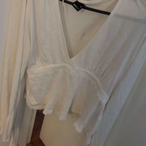 Vit omlottblus med v-ringning - Säljer en vit blus från Gina Tricot med snygg omlottdesign och djup v-ringning. Blusen har långa ärmar och är tillverkad i ett lätt, mjukt material som ger en skön känsla. Perfekt för dig som gillar en feminin och stilren look. Liten fläck innuti som ej syns utrifrån