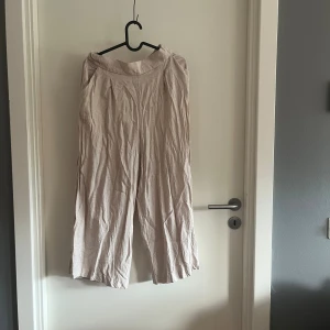 Beige linnebyxor från H&M, strl 38 - Säljer ett par ljusbeige linnebyxor från H&M i storlek 38. Byxorna har en relaxed passform med breda ben och resår i midjan. 
