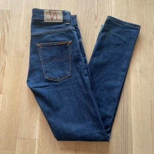 Mörkblå Nudie Jeans Grim Tim W29 L32 - Jag säljer dom här riktigt feta Nudie Grim Tim jeansen som är i storlek W29 L32. Dom är använda men fortfarande i bra skick. Tveka inte att höra av er!                                                                Mått: Längd=99cm. Midja=37cm