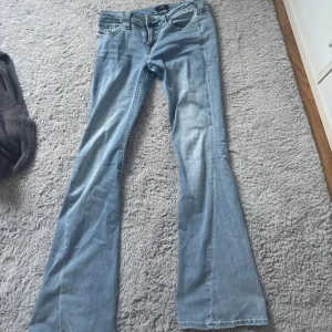 True Religion Joey ljusblå flare jeans - Säljer ett par ljusblå True Religion Joey jeans med låg midja och snygg flare. Klassiska femficksmodellen med coola detaljer på bakfickorna och ikonisk patch bak. Perfekt för dig som gillar retrovibbar och statement-jeans.