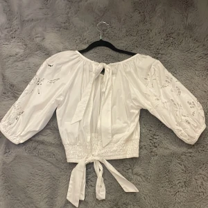 Vit broderad blus från Gina Tricot - Superfin vit blus från Gina Tricot med broderade detaljer och cut-outs på ärmarna. Blusen har trekvartsärmar, knytband bak samt smockad midja för en snygg passform. Aldrig använd. Pris kan diskuteras. 