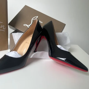 Svarta Louboutin pumps med röd sula - Säljer ett par ikoniska svarta pumps från Christian Louboutin med glansig finish och klassisk röd sula. Skorna har spetsig tå och hög klack, tillverkade i lackat skinn. Perfekta för dig som vill ha en elegant och edgy look.