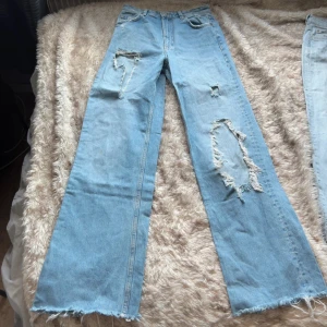Ljusa ripped jeans från Zara, strl 36 - Säljer ett par ljusblå jeans från Zara i storlek 36. Jeansen har breda, raka ben och flera slitningar och hål. Liten fläck på högra knät. innerbenslängd 86 cm.