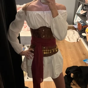 Hel pirat kostym  -  Säljer hela min pirat kostym då jag ångrade mig man får med en lång rad sjal guldbälte brun korsett ett sätt med en vit tröja och en vit kjol. Kjolen knyter du själv och sen Sånna saker du sätter i en fläta se på bild 2 (allt är i storlek xs) du kan bara köpa hela kostymen pris kan diskuteras men köpte allt för 550kr och postar direkt 