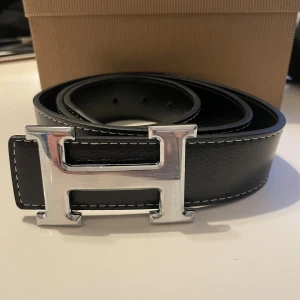 Svart bälte - svart bälte med silvrigt H spänne. 110cm långt