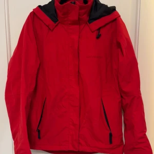 Röd vindjacka från Everest storlek S - Jättefin Everest jacka med smarta fickor och fräsch röd färg. Kan användas som vindjacka eller skidjacka med något varmt under. Försiktigt använd så den är i väldigt bra skick
