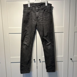 Levi's 502 mörkgrå jeans, W30 L - Snygga Levi's 502 Hi-Ball jeans i mörkgrå tvätt med klassisk femficksdesign och raka ben. Jeansen har en normal passform och är tillverkade i slitstarkt denim med subtila slitningar för en cool look. Perfekt för dig som gillar stilrena och tidlösa jeans.