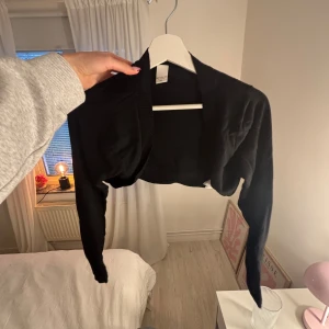 Svart bolero - Svart bolero från Vila med långärmad design och ribbad kant vid halsen och nederdelen. Perfekt att slänga över en topp för en chill look. Mjuk och tunn i materialet!💖