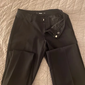 Svarta kostymbyxor från Bik Bok - Klassiska svarta lågmidjade kostymbyxor från Bik Bok med diskreta fickor. Byxorna har hällor för bälte, knapp och dragkedja i midjan. Perfekta för en clean och stilren look. Jag väljer att sälja dessa då de inte kommer till användning längre. Kvaliten är mycket bra, inget slitage. 
