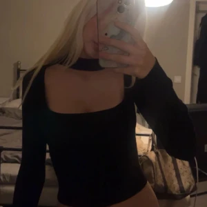 Svart långärmad topp med choker - Säljer en svart långärmad topp med fyrkantig urringning och inbyggd choker-detalj runt halsen. Sitter tight och har en stilren, modern look som passar perfekt till jeans eller kjol.