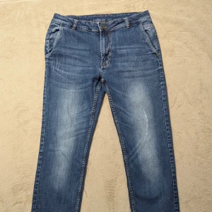 Blå jeansbyxor från Piazza Italia - Snygga blå jeansbyxor från Piazza Italia i storlek 48. Byxorna har klassisk femficksdesign, bälteshällor och subtila slitningar framtill. De är tillverkade i mjukt jeanstyg och har en rak passform som ger en clean look. De är köpta i Italien 🇮🇹 och är ganska unika att hittas! 