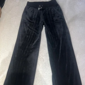 Svarta mjukisbyxor i sammet juicy couture - Svarta mjukisbyxor från Juicy Couture i mjuk sammet med bred resår och snörning i midjan. Byxorna har raka, vida ben och stora fickor både fram och bak. Perfekta för en chill och trendig look. Använda 3-4 gånger