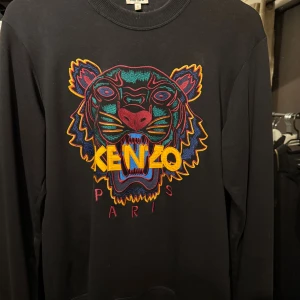 Svart Kenzo sweatshirt med tigerbroderi - Svart sweatshirt från Kenzo. Det är en ikonisk tröja från kenzo som sticker ut.                                                   Storlek: S men sitter som en M  Pris kan diskuteras vid snabbaffär