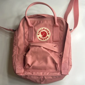 Rosa Kånken Axelrämväska från Fjällräven - Säljer en rosa Kånken Mini ryggsäck från Fjällräven med klassisk rund logga framtill. Väskan har ett huvudfack med dragkedja, ett mindre ytterfack och justerbara axelremmar. Perfekt storlek för det viktigaste och har både handtag och ryggsäcksremmar. Den är knappt använd. Har använt den 1-2 gånger själv. Köpte när jag var lite yngre. Har ingen användning av den och det är anledningen till varför jag säljer den! Priset kan diskuteras. 