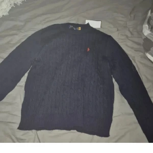 Rl stickad  - stickad mörkblå tröja från Polo Ralph Lauren med rund halsringning och den klassiska röda logotypen broderad på bröstet. Tröjan har ribbade muddar vid ärmslut och nederkant. Perfekt för lager på lager och en stilren look.