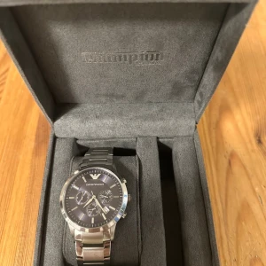 Emporio Armani silverfärgad klocka - Stilren klocka från Emporio Armani med silverfärgad länk i metall och mörk urtavla. Klockan har flera små urtavlor, datumvisning och klassisk design. Levereras i originalbox med märkets logga. Perfekt accessoar för dig som gillar snygga detaljer. Pris kan diskuteras.