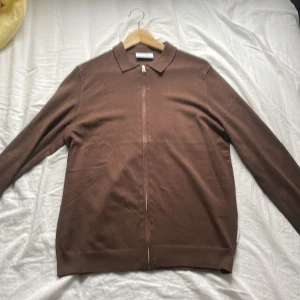 Brun kofta med dragkedja Only & Sons - Brun kofta från Only & Sons med klassisk krage och hel dragkedja framtill. Långärmad och i mjukt material med 78% viskos. Perfekt för lager-på-lager och enkel att matcha med jeans eller chinos.