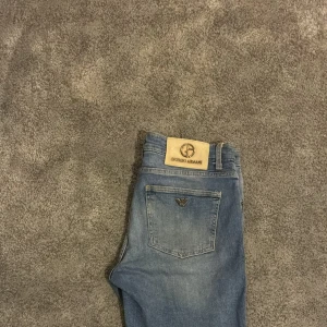 Blå jeansshorts från Giorgio Armani - Snygga blå jeansshorts från Giorgio Armani med klassisk femficksdesign och ikoniska logodetaljer på knapp och bakficka. Shortsen har en rak passform och är tillverkade i mjuk bomull. Perfekta för dig som gillar stilrena och exklusiva plagg.