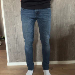 Nudie Jeans – Slim Fit Blue Denim - Klassiska blå jeans från Nudie Jeans i en slim fit-passform. Mjuka, stretchiga och bekväma med snyggt sliten tvätt.   ✔️ Storlek: W30 L32  ✔️ Modell: Slim Fit ✔️ Färg: Mellanblå denim ✔️ Skick: Bra använt skick, inga hål eller fläckar