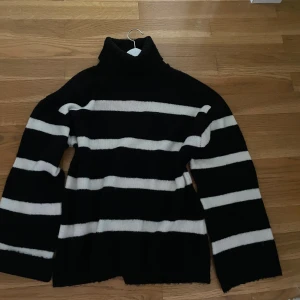 Randig svartvit polotröja - Säljer en svart och vit randig polotröja med. Tröjan har hög krage och långa ärmar, perfekt för kyliga dagar. Den är stickad och har en klassisk, avslappnad passform.