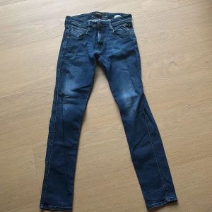 Blå skinny jeans från Replay - Snygga blå jeans från Replay med klassisk femficksdesign och tydliga slitningar framtill. Jeansen har smal passform och raka ben, med detaljerade sömmar och läderpatch bak i midjan. Perfekta för dig som gillar en modern och stilren look.