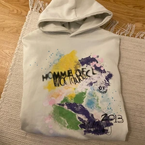 Vit hoodie med snyggt tryck - Vit hoodie från Homme De Couleur med färgstänk samt coolt tryck och graffiti-liknande detaljer både fram och bak. Oversized passform med huva för en chill vibe. 