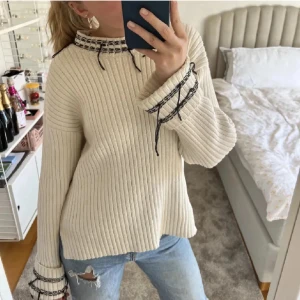 Beige ribbstickad tröja med snörning - Superfin beige ribbstickad tröja med svarta snörningsdetaljer vid halsringning och ärmslut. Tröjan har en loose passform och långa ärmar, perfekt för lager på lager. Snygg till jeans eller kjol för en chill look.(obs inte mina bilder)