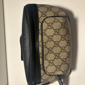 Gucci väska med GG-mönster - Snygg axelväska från Gucci i beige och svart med klassiskt GG-mönster. Väskan har justerbar axelrem, svart skinn-detaljer och dragkedja. Perfekt storlek för det viktigaste och ikonisk design som sticker ut.