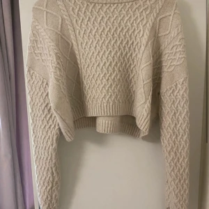 Beige stickad croppad tröja H&M - Superfin beige stickad tröja från H&M med grovt flätmönster och ribbade muddar. Modellen är croppad och har lång ärm, perfekt för lager-på-lager under kyliga dagar. Snygg till både jeans och kjol!