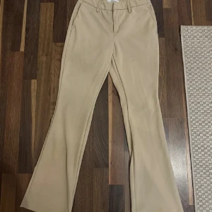 Beiga bootcut kostymbyxor veromoda - Snygga beiga kostymbyxor med bootcut-snitt och klassisk passform. Byxorna har hällor för bälte och stängs framtill. Perfekta för en stilren look och lätta att matcha med olika toppar.