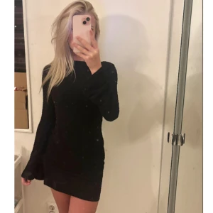 Svart figurnära kortklänning - Supersnygg svart kortklänning med lång ärm och tight passform. Klänningen har en strukturerad yta som ger en cool look och markerar midjan. Perfekt för dig som gillar minimalistisk stil med edge.