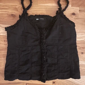 Svart linnetopp  - Svart linnetopp från Zara med fransade kanter. Toppen har smala axelband och knappar framtill. 