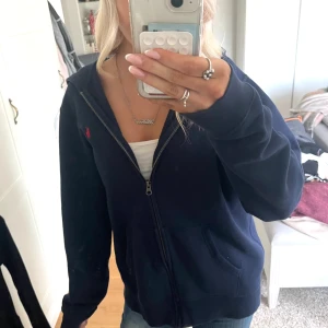 Mörkblå hoodie från Polo Ralph Lauren - Säljer en mörkblå hoodie från Polo Ralph Lauren i storlek XL. Tröjan har dragkedja framtill, huva och fickor på sidorna. Klassisk röd logga broderad på bröstet. Endast andvänd ett fåtal gånger! 