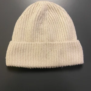 Krämvit ribbstickad mössa från H&M - Snygg ribbstickad mössa i beige från H&M. Klassisk modell med uppvikt kant och mjukt material som håller dig varm. Perfekt accessoar för kyliga dagar och enkel att matcha med olika outfits! 