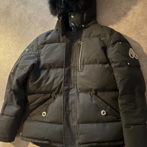 Svart dunjacka från Moose Knuckles - Säljer en svart dunjacka från Moose Knuckles med pälskantad huva, flera dragkedjefickor och snygga metalldetaljer