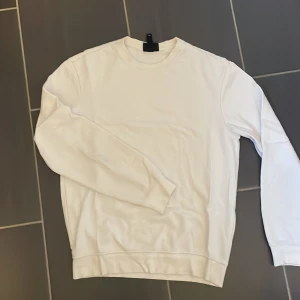 Vit sweatshirt från H&M relaxed fit - Vit sweatshirt från H&M i relaxed fit. Tröjan har rund hals, långa ärmar och ribbade muddar vid hals, ärmslut och nederkant. Tillverkad i mjuk bomull som är skön mot huden. Enkel och clean design som funkar till många olika stilar.