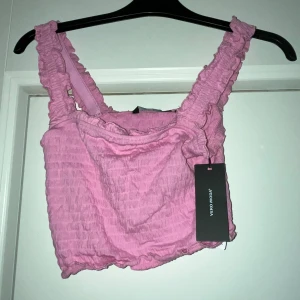 Rosa croppad linnetopp Vero Moda XS - Säljer en söt rosa croppad linnetopp från Vero Moda i storlek XS. Toppen har breda, rynkade axelband och ett smockat tyg som ger en cool struktur. Perfekt för sommarens alla häng! Taggen sitter kvar.