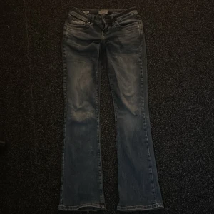 Blå bootcut jeans från LTB - Snygga blå jeans från LTB, modell Valerie. Bootcut passform med klassisk femficksdesign och slitna detaljer för en cool look. Jeansen har låg midja och är tillverkade i jeansmaterial med dragkedja och knapp framtill. Storlek 25/32